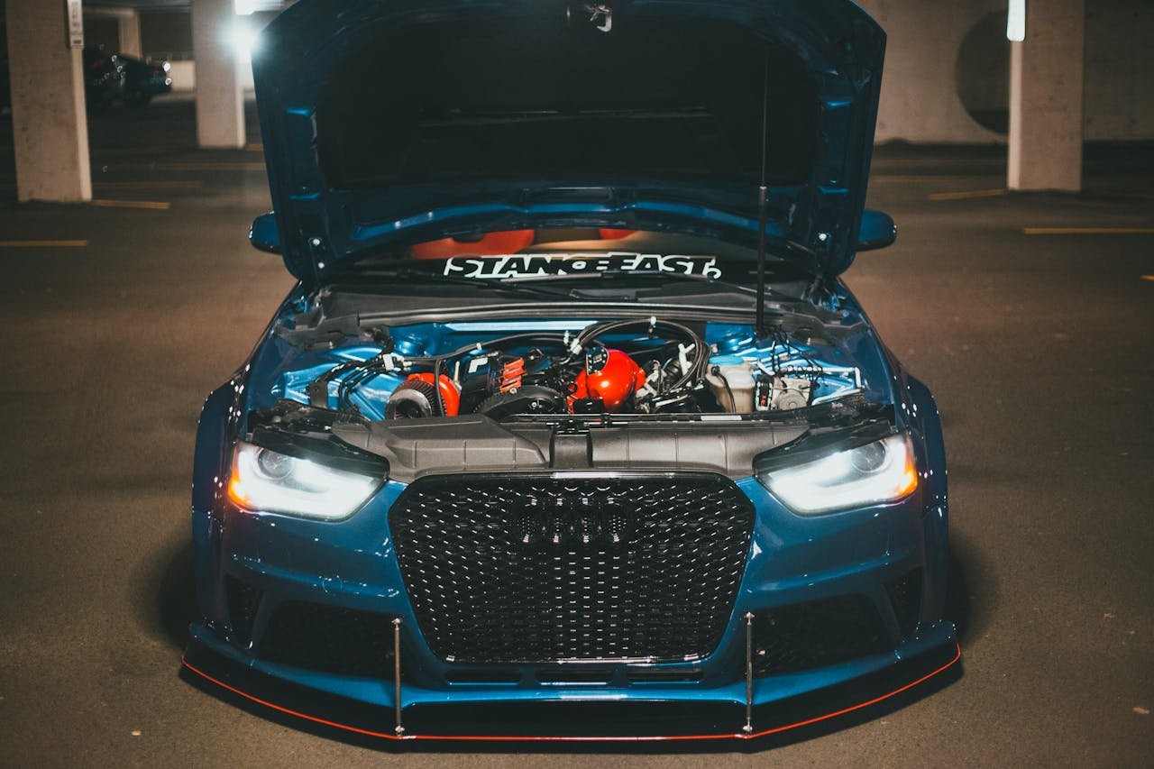 Blue sports car with open hood displaying engine in dimly lit urban setting.